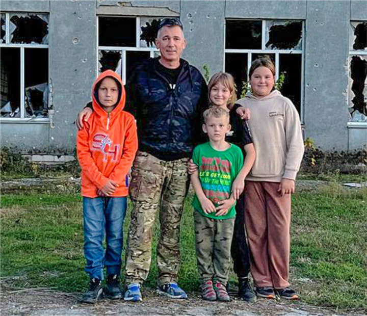 Marek Wnuk mit ein paar Kindern vor einer zerstörten Schule.